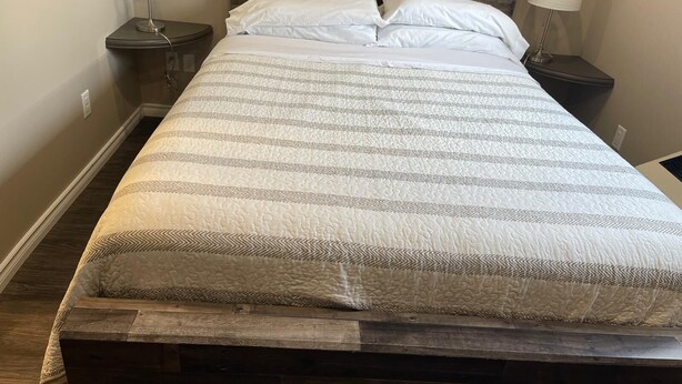 Een net opgemaakt bed met een gestreept dekbedovertrek, twee nachtkastjes met lampen en een houten hoofdbord.