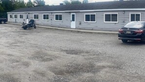 Een motel met een laag gebouw, een parkeerplaats met grind en een zwarte auto ervoor.