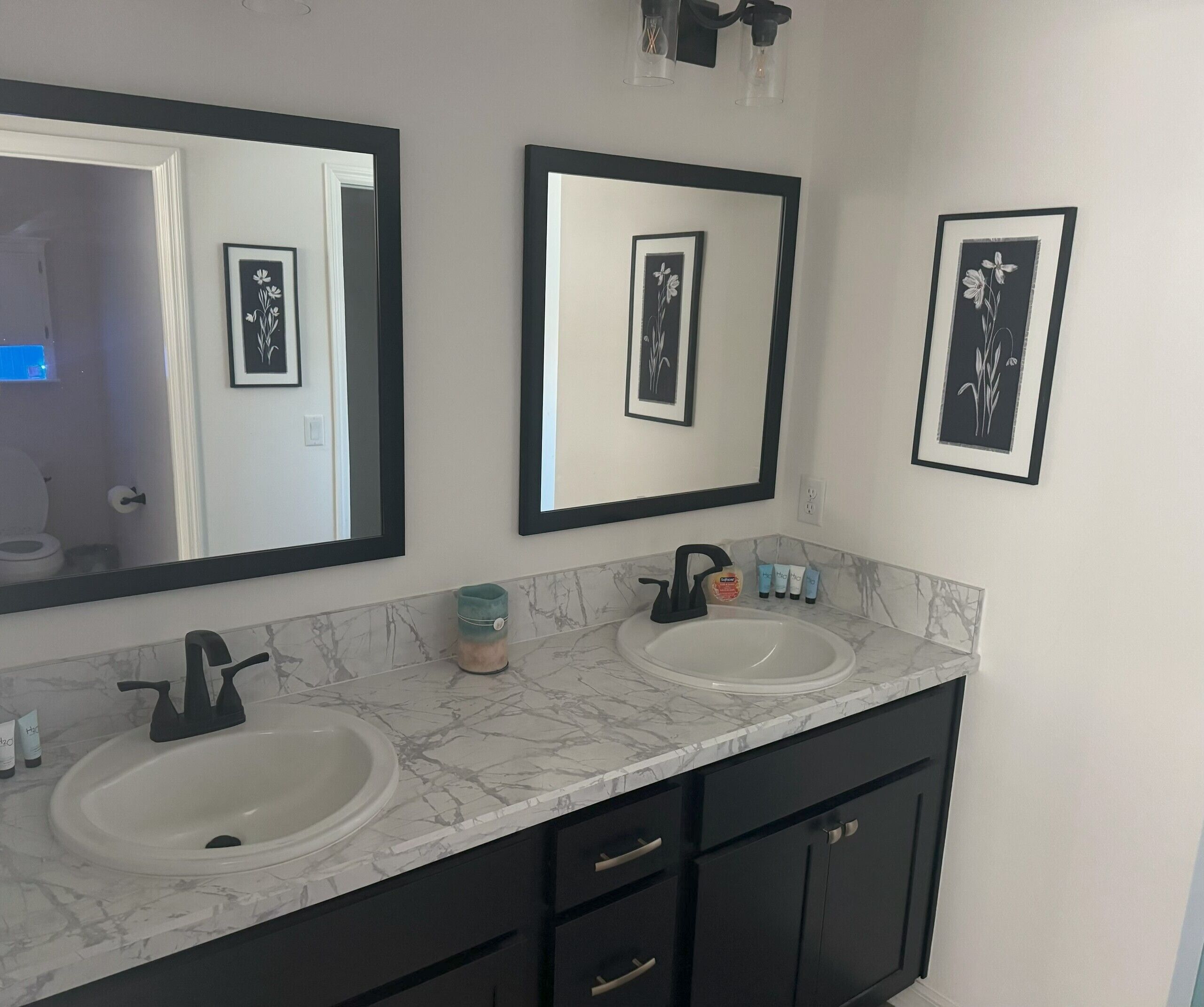 Une salle de bain avec deux lavabos, des meubles noirs et trois tableaux encadrés accrochés au mur.