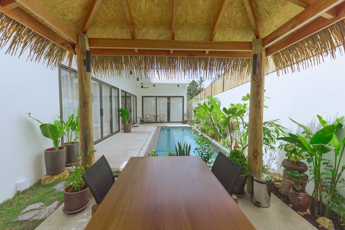 Un espace extérieur abrité comprenant une piscine, une table en bois, des chaises et des plantes en pot.