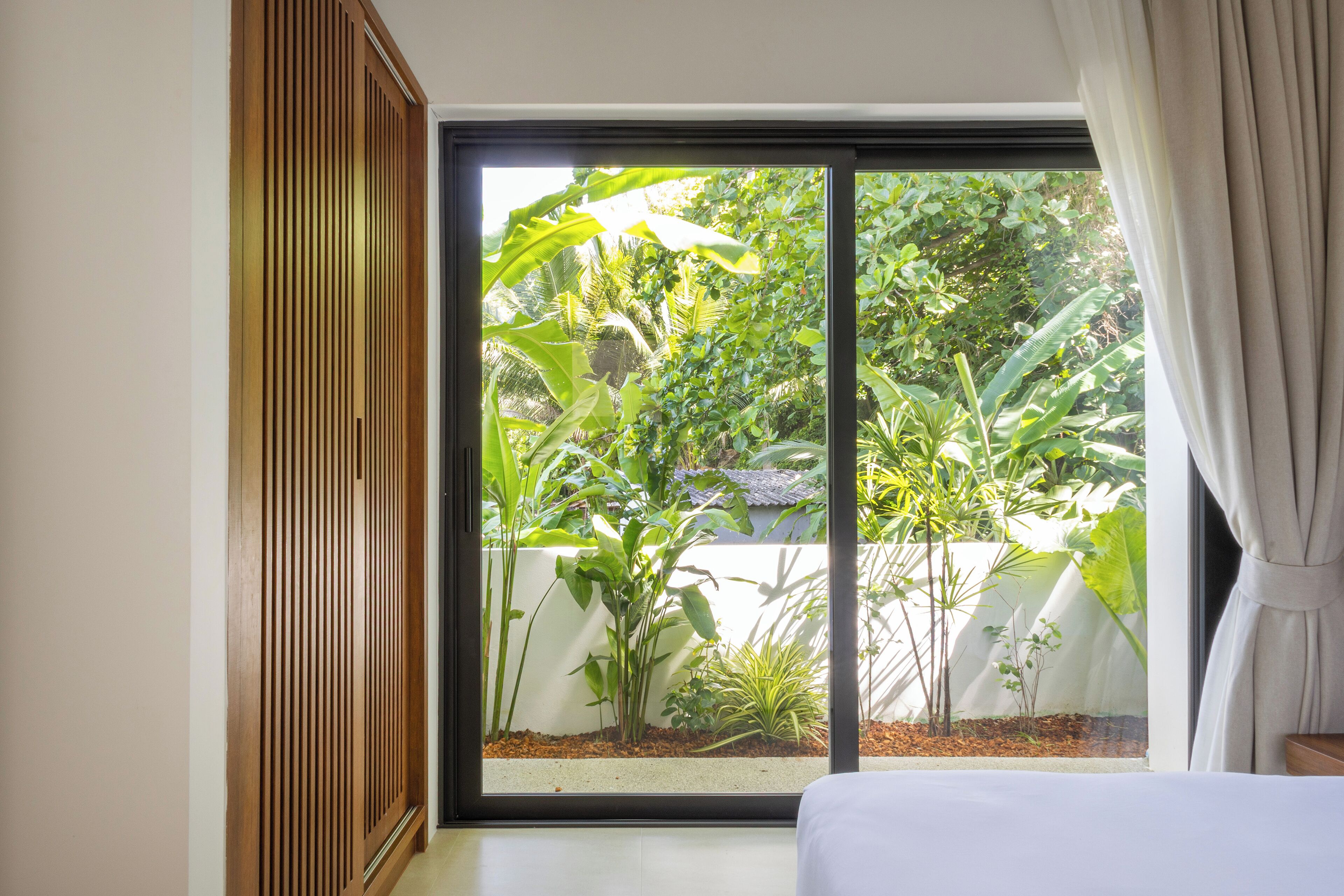 A room with a large sliding glass door leading to a garden with various plants.