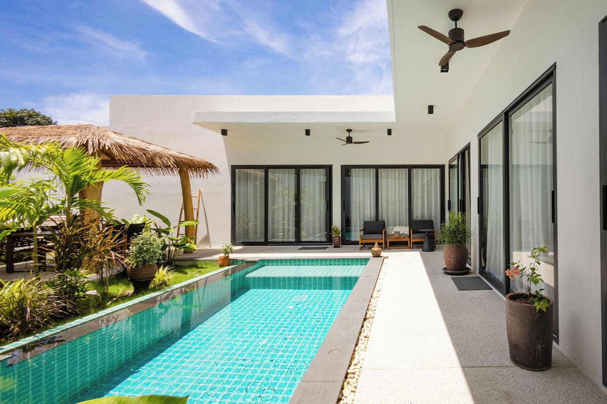 Une maison moderne dotée d’une piscine, de grandes fenêtres et d’un patio agrémenté de plantes.