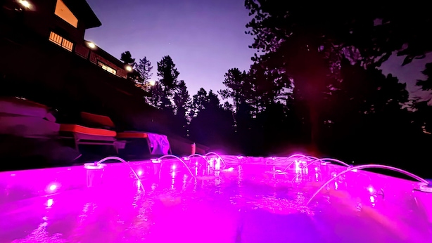 Ein Schwimmbad mit einer Wassersäule und violetter Beleuchtung bei Nacht.