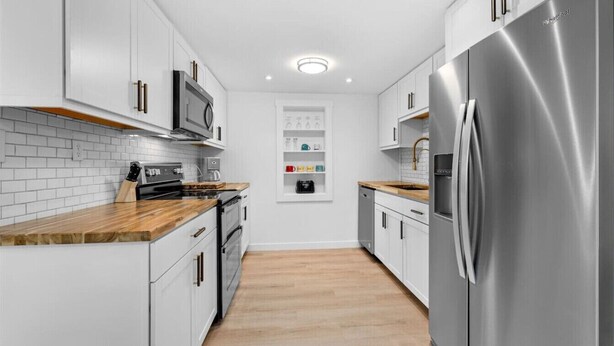 A modern kitchen with white cabinetry, stainless steel appliances, and wooden countertops. - Coastal 2-Bedroom Home Minutes to Beach (Englewood)