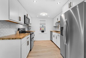 A modern kitchen with white cabinetry, stainless steel appliances, and wooden countertops. - Coastal 2-Bedroom Home Minutes to Beach (Englewood)