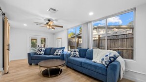 A spacious living room with a large window, a ceiling fan, and a wooden floor. - Coastal 2-Bedroom Home Minutes to Beach (Englewood)