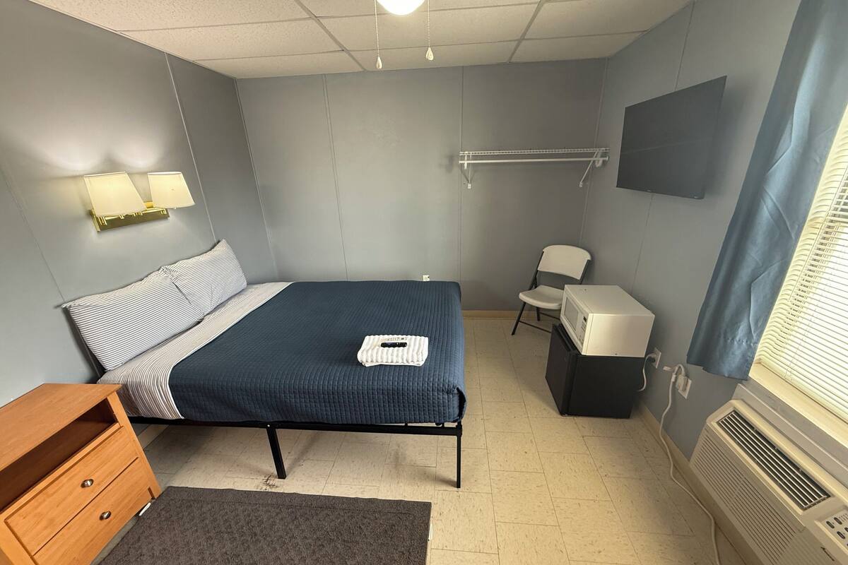 A bedroom with a bed, bedside table, chair, TV, and heater.