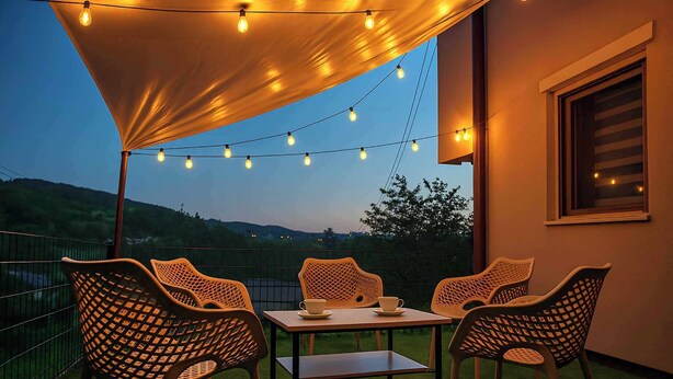 Een terras buiten met een tafel, stoelen, lichtjes en uitzicht op de heuvels.