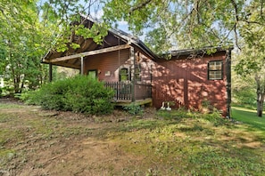 A rustic cabin with a wooden porch, surrounded by dense greenery and trees. - Patoka Lake, Stones Throw Cabin (Birdseye)