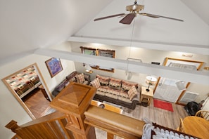 Un vaste espace de vie doté d’un haut plafond, d’un ventilateur de plafond, d’un ensemble de canapés, d’une table basse en bois et d’un escalier menant à un niveau supérieur.