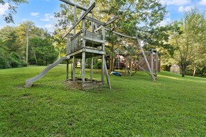Une structure de jeux en bois, avec un toboggan et des balançoires, installée dans une cour gazonnée.