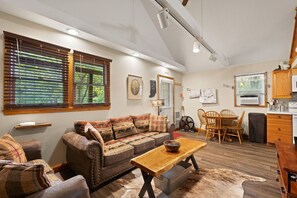 Un salon chaleureux avec un canapé, une table basse en bois et un coin repas comprenant une table et des chaises. Il y a également une cuisine équipée de placards et d’un réfrigérateur.