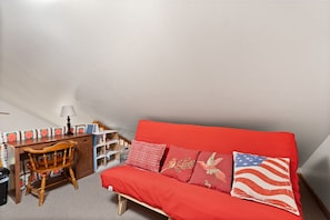 Une pièce chaleureuse avec un canapé rouge, une chaise en bois, un bureau et une lampe.