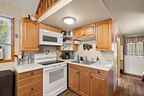 A compact kitchen with wooden cabinets, a microwave, stove, and sink.