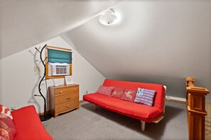 A small, cozy room with a sloped ceiling, a red sofa, a wooden dresser, and a wall-mounted radiator.