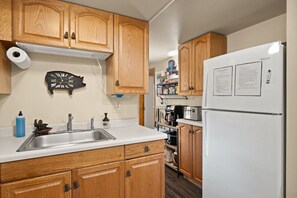 Une cuisine avec des meubles en bois, un évier en acier inoxydable, un réfrigérateur blanc et une horloge au mur.