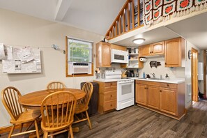 Une cuisine compacte avec des meubles en bois, une cuisinière blanche et un four à micro-ondes. On y trouve une table à manger avec des chaises et une carte accrochée au mur.