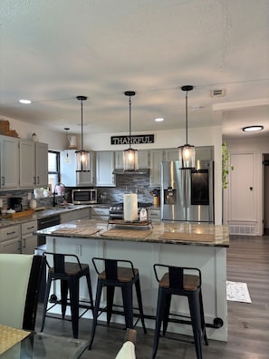 A modern kitchen with a central island, bar stools, stainless steel appliances, and pendant lighting.