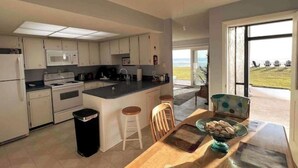 Una cocina moderna con armarios blancos, una isla central y vistas al océano a través de amplios ventanales.