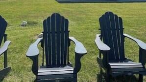 Un edificio moderno de dos plantas con balcón, rodeado de césped y dos sillas Adirondack.