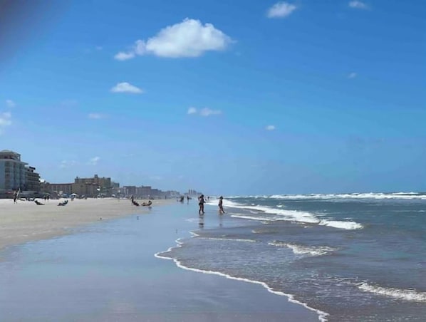 Ein Strand mit blauem Himmel, Wellen und Gebäuden im Hintergrund.