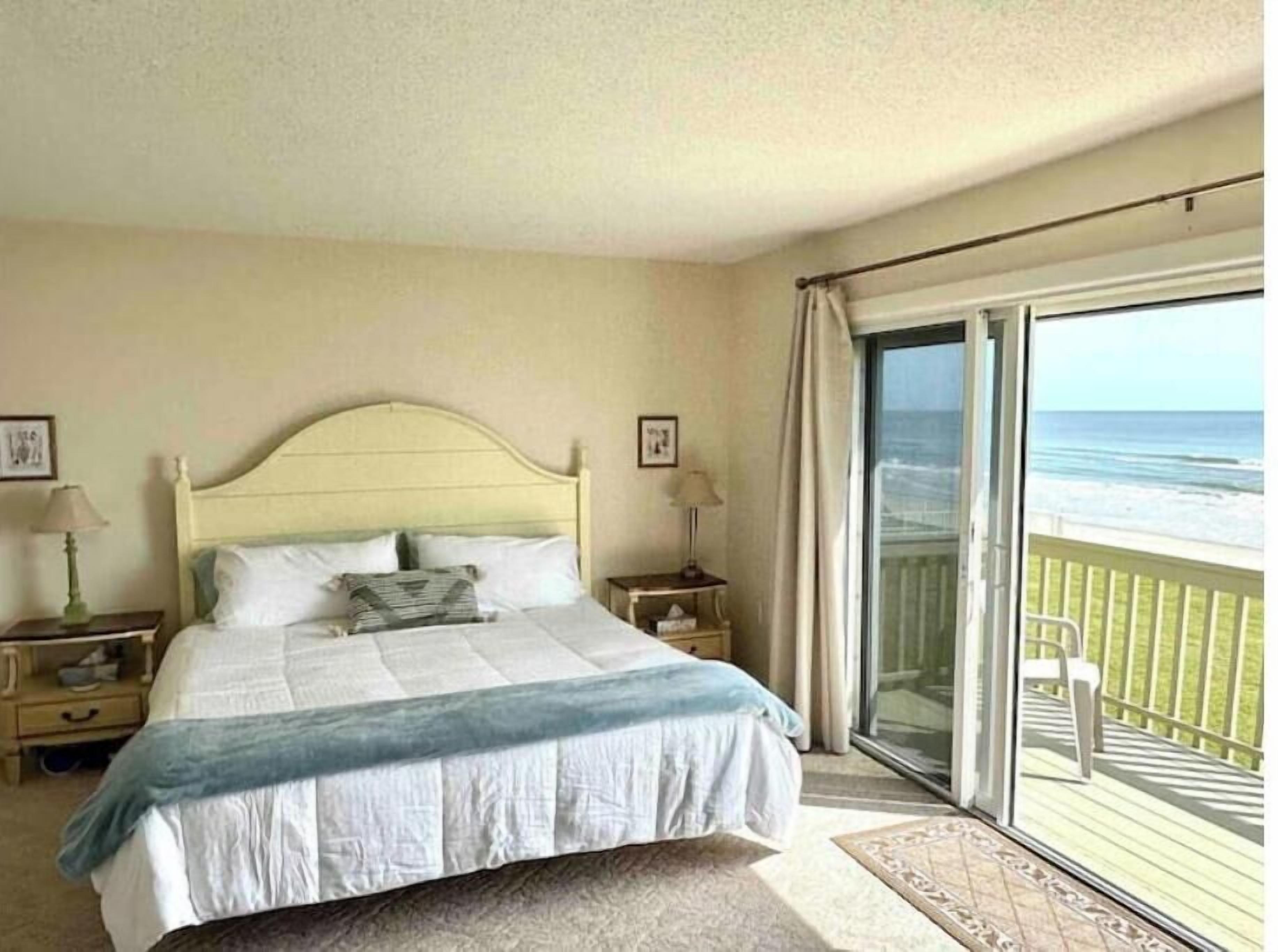 A bedroom with a bed, nightstands, a window with a view of the beach, and a balcony.