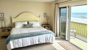 Un dormitorio con cama, mesitas de noche, una ventana con vista a la playa y un balcón.