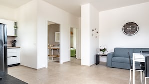 A modern living room with a grey sofa, a dining table, and a kitchen area in the background. - Apartment 'Flora' with Private Garden, Wi-Fi, and Air Conditioning (Cisternino)