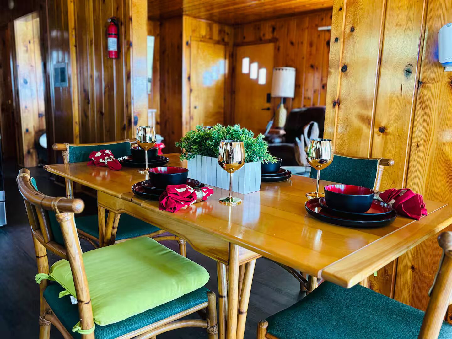 A wooden dining table with chairs, a fire extinguisher on the wall, and a small potted plant on the table.