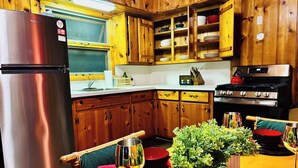 Una cocina con armarios de madera, un refrigerador de acero inoxidable, una estufa y una mesa de comedor con sillas rojas y una planta en maceta.