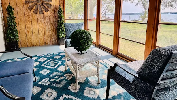 Una habitación acogedora con un ventanal grande, un muro de madera, un dardo y una alfombra estampada.