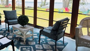 Una habitación con ventanas amplias, mobiliario de mimbre y vistas a un área verde con sillas afuera.