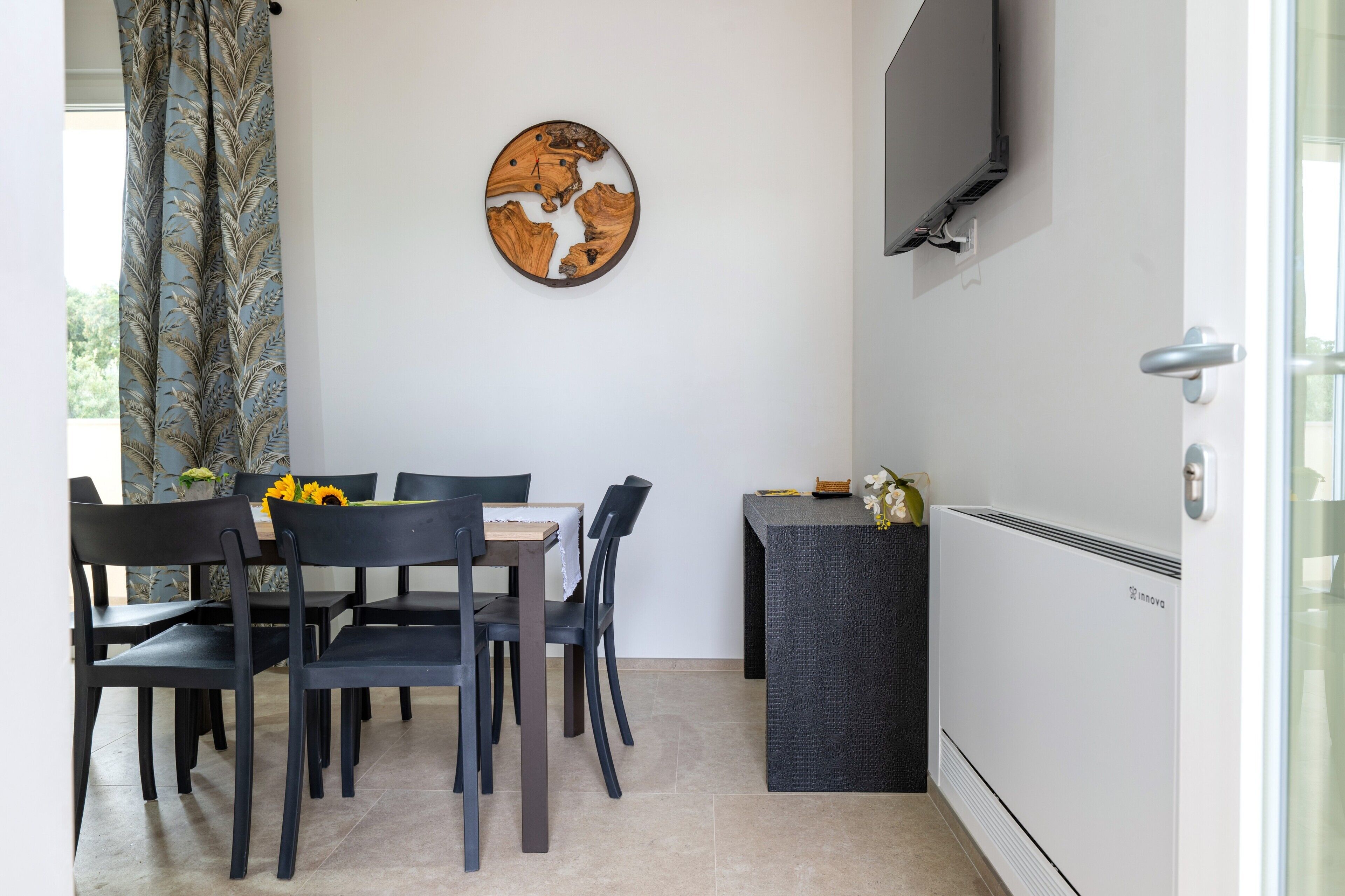 A dining area with a table and chairs, a wall-mounted TV, and a radiator.