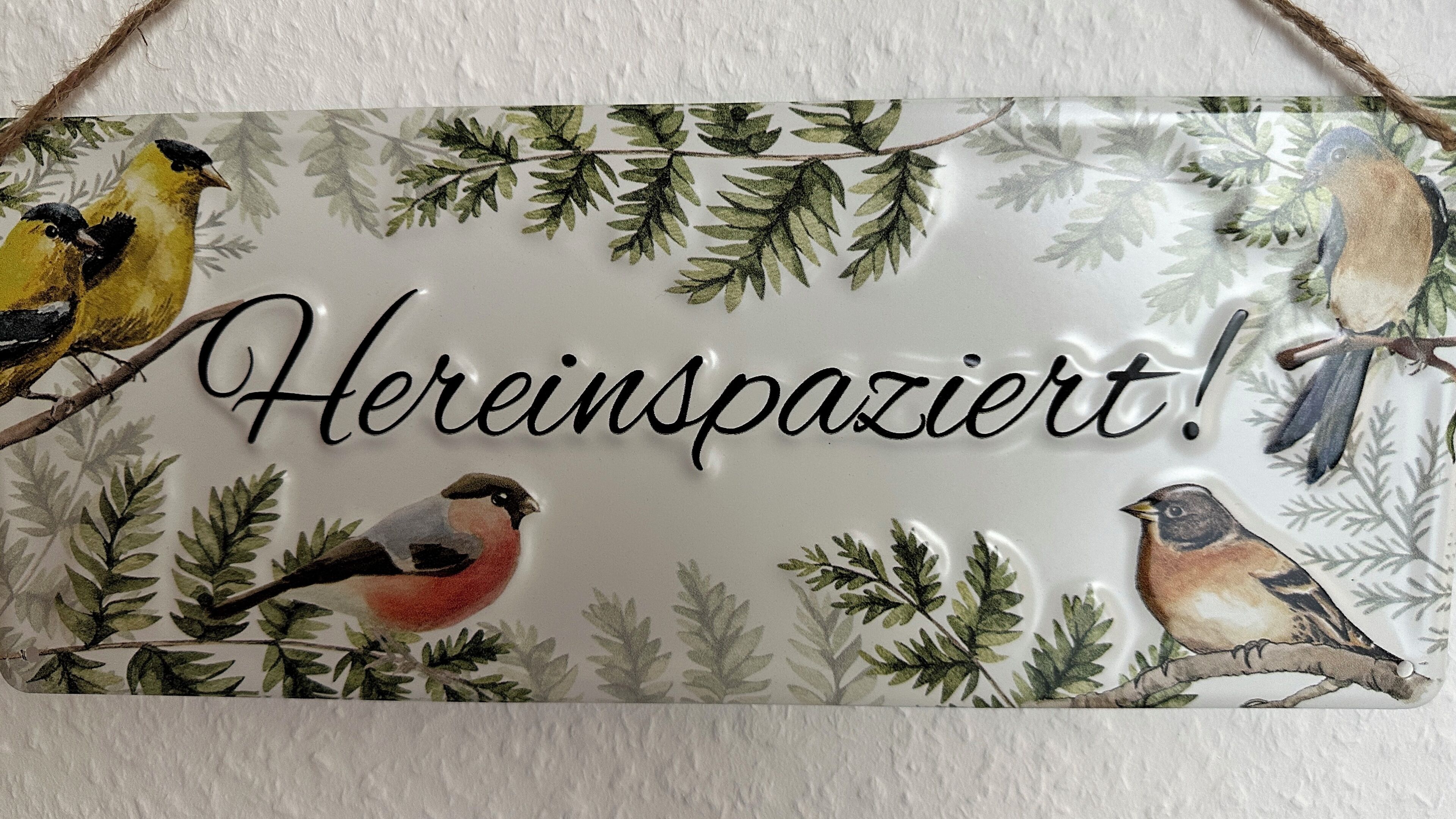 Une enseigne décorative représentant des oiseaux et portant l’inscription « Hereinpaziert ! »