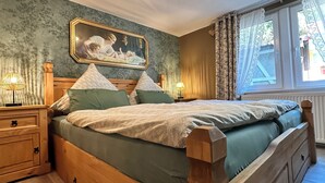 A bedroom with a wooden bed, green bedding, a nightstand with a lamp, a painting on the wall, and a window with curtains. - Harz-Bleibe Wernigerode, very centrally located. (Wernigerode)