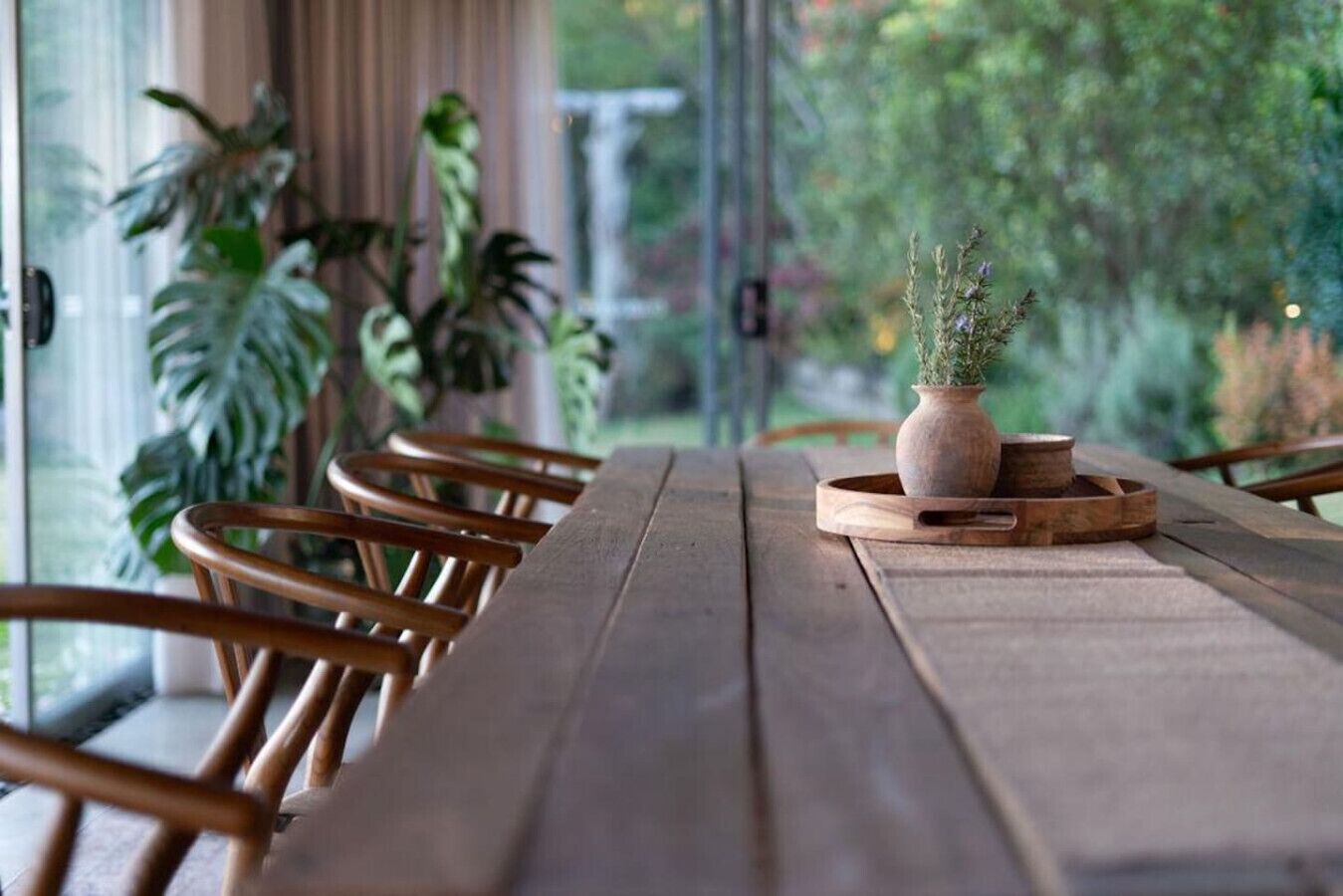 Una mesa de madera con sillas, una planta en maceta y una ventana que da a zonas verdes.