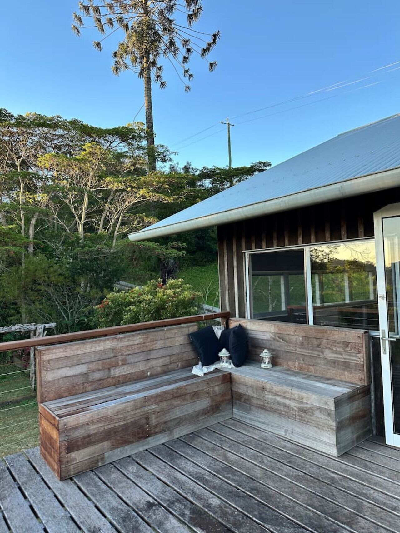 A wooden deck with a built-in bench, a glass door, and a view of the surrounding greenery.