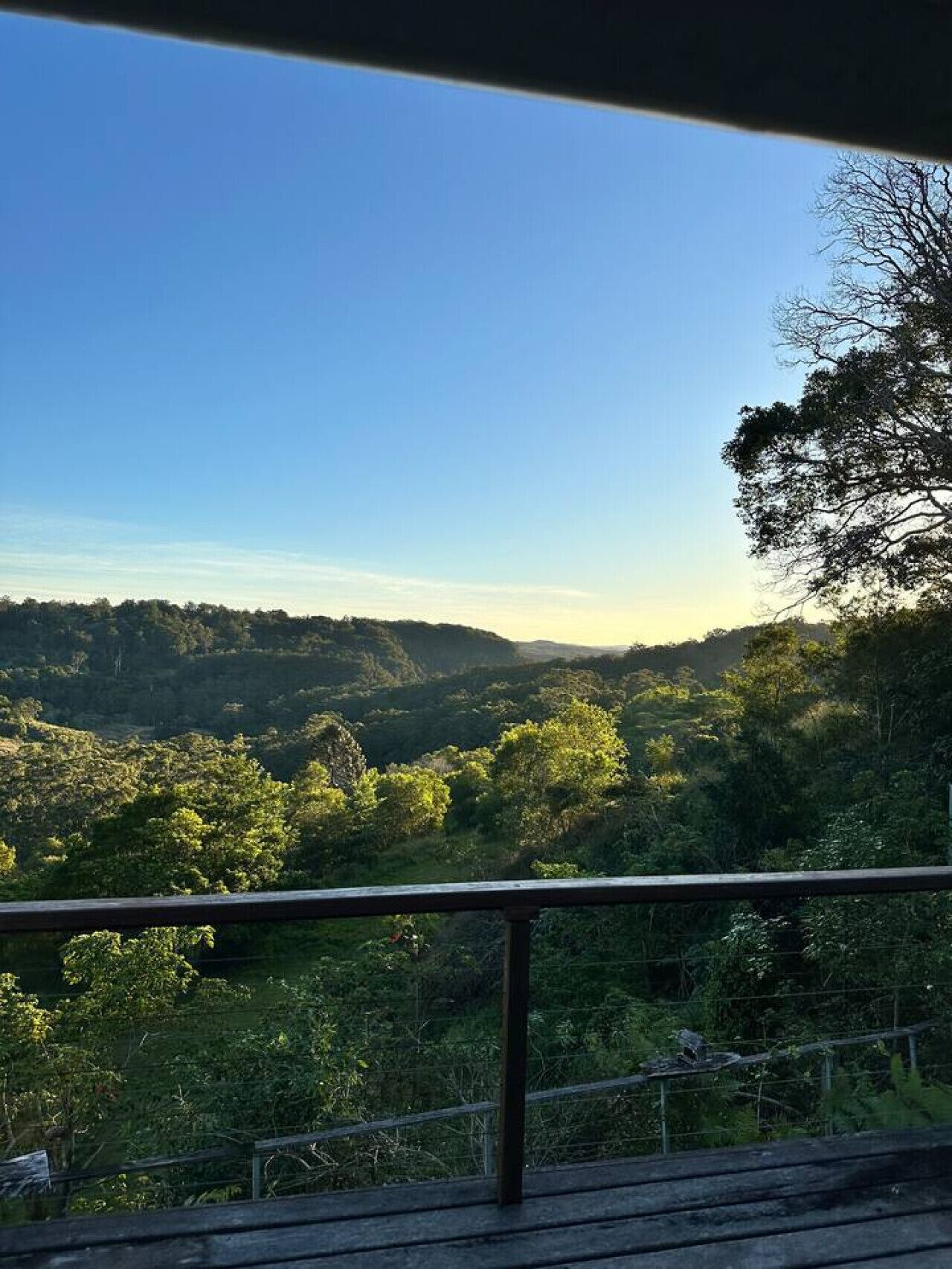 Vista de varanda sobre um vale verdejante e céu claro.