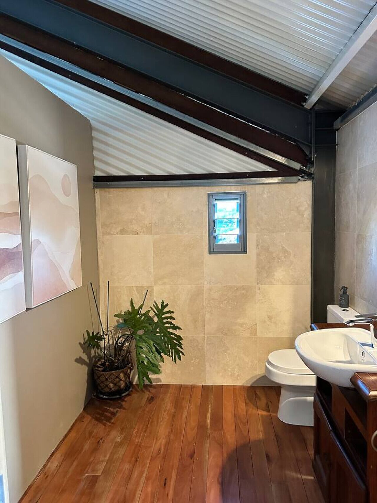 Ein Badezimmer mit Holzboden, Toilette, Waschbecken, Fenster und einer Topfpflanze.