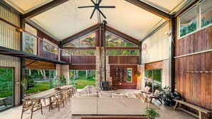 A spacious living area with a high ceiling, a fireplace, and a view of the outdoors.