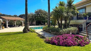 A well-maintained garden with a swimming pool, palm trees, and a gazebo.