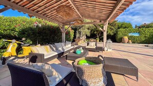 An outdoor patio with wicker furniture, a yellow scooter, and a pergola with a woven ceiling.