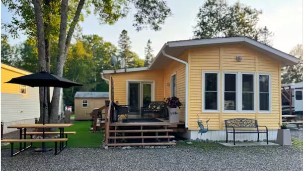 Una casa móvil amarilla con un porche, una pequeña terraza y una mesa de picnic.