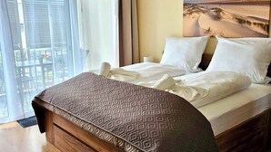 A bedroom with a bed, a painting of a desert landscape, and a view through a window. - Südwind 05 - apartment, close to the beach, swimming pool, sauna, parking, WLAN, and balcony (Zempin)