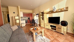 A living room with a sofa, a coffee table, a TV, and a kitchen in the background. - Südwind 05 - apartment, close to the beach, swimming pool, sauna, parking, WLAN, and balcony (Zempin)