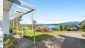 A residential property with a covered patio, a view of a lake, and a mountain in the background. - Nestle In Narooma - 10 Hillcrest Ave North Narooma (North Narooma)