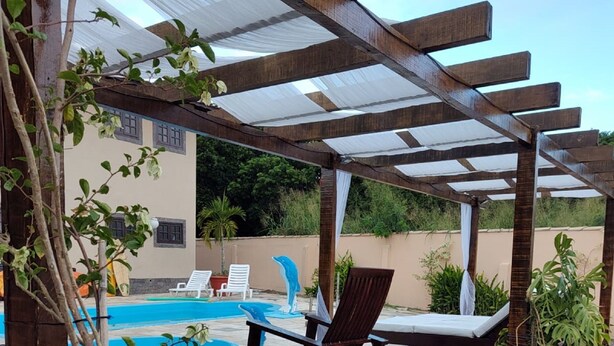 A wooden deck with a pergola, a pool, lounge chairs, and potted plants. - Aruna Eco Pousada (Buzios)
