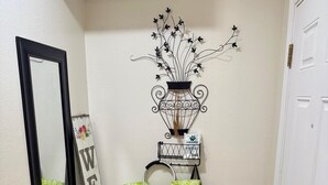 A hallway with a mirror, a welcome sign, a metal wall decoration, a bench, and a potted plant.