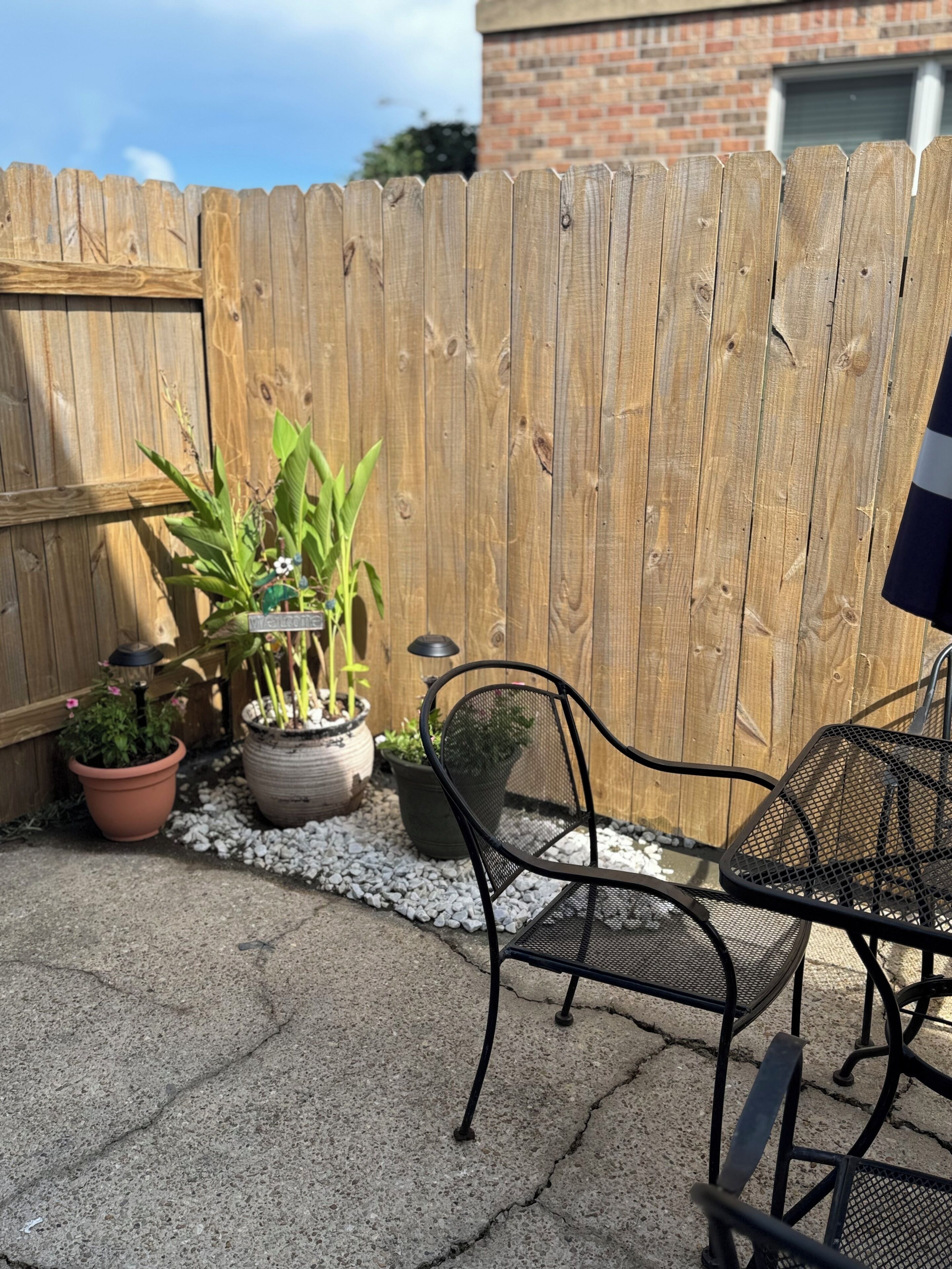 A patio area with a wooden fence, potted plants, and metal chairs.