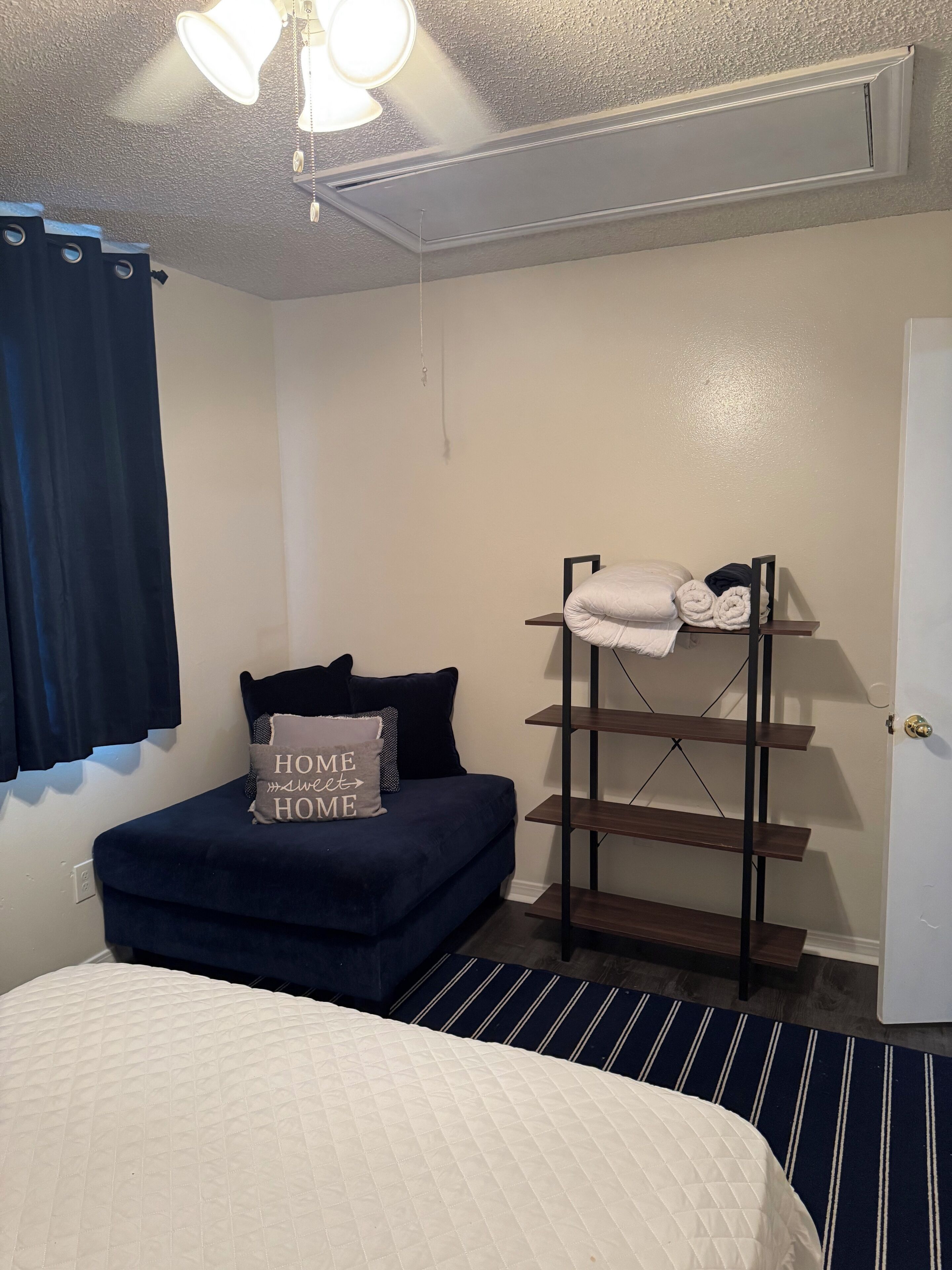 Une chambre avec un lit, un petit canapé, une étagère avec des serviettes et un ventilateur de plafond.